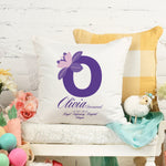 White pillow with a purple letter 'O' and floral design on a white surface with decorative items.