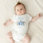 Baby wearing a white onesie with blue floral design and text on a beige blanket