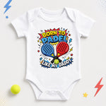 White “Born to padel like my Daddy” baby bodysuit with blue and red rackets and colourful comic-style lettering.