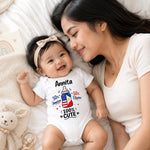A baby lying on a white blanket next to a smiling woman, wearing a white bodysuit with a colorful graphic of a baby bottle and the text 'Annita 50% Americano 50% Filipino 100% CUTE'.