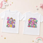 Two white short-sleeve baby t-shirts shown flat on a light beige background, displaying the front and back designs. The front features a colorful cartoon unicorn and balloons with the text 'Sophia turns one'.