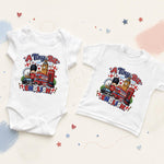 A white baby bodysuit and a white toddler T-shirt laid flat on a light cream background with pastel paint strokes and small star accents. Both garments feature a colorful graphic print reading “A Tiny Bit of ENGLAND” with a cartoon bear, red double-decker bus, London Eye, and London flags.