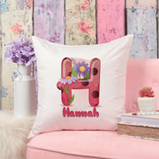 Decorative pillow with a floral letter 'H' and name 'Hannah' on a pink couch with a floral wall background.