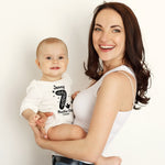 Woman holding a baby wearing a '7 months old' shirt against a plain background