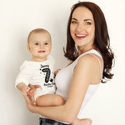 Woman holding a baby wearing a '7 months old' shirt against a plain background