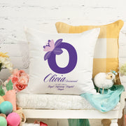 White pillow with a purple letter 'O' and floral design on a white surface with decorative items.