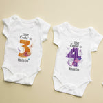 Two baby onesies with milestone text on a beige background