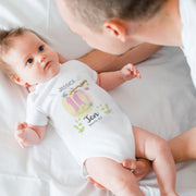 Baby wearing a onesie with personalized design, held by an adult on a white background