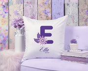 Decorative pillow with a purple letter 'E' and floral design on a floral-patterned wall background.