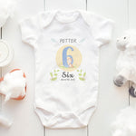 Baby onesie with 'Petter' and 'Six Month Old' text on a white wooden surface