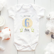Baby onesie with 'Petter' and 'Six Month Old' text on a white wooden surface