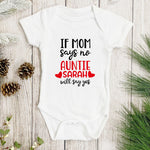 White baby onesie with text on a wooden surface with pine cones and greenery