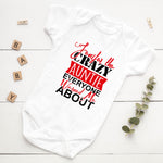 White baby onesie with red and black text on a white wooden surface with decorative elements.