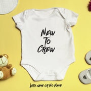 White baby onesie with 'New To Crew' text on a yellow background
