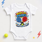 White “Born to padel like my Daddy” baby bodysuit with blue and red rackets and colourful comic-style lettering.