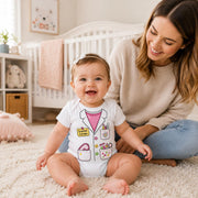 A baby wearing a white doctor-themed bodysuit sits on a cream shag rug next to a smiling woman in a cozy nursery setting.