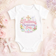 White personalised christening day baby bodysuit with pink lettering, name and date, cross and floral decorations.