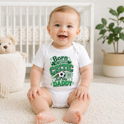 Smiling baby wearing a white “Born to support Celtic just like Daddy” bodysuit with green lettering and football.