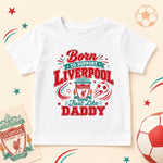 White Liverpool T-shirt with “Born to support Liverpool just like Daddy”, red and teal lettering and club crest.