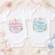 Two white personalised christening bodysuits with pink and blue lettering, names, dates, crosses and flowers.