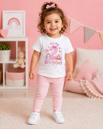 Child wearing a white second birthday T-shirt with a pink number 2, unicorn and princess carriage, with pink trousers.