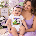 Woman holding a smiling baby in a personalised 4 months old panda bodysuit beside milestone signs and balloons.