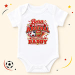 A white short-sleeve baby bodysuit with a colorful graphic print that reads 'Born to Support Arsenal Just Like Daddy' with the Arsenal FC crest and soccer ball motif, displayed on a light beige background with decorative soccer-themed doodles.