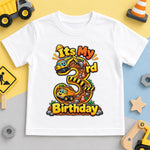 White third birthday T-shirt with a large number 3 and colourful construction trucks, beside toy vehicles.