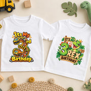 Two white third birthday T-shirts showing colourful construction truck and green dinosaur designs.