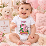 Smiling baby wearing a personalised 7 months old safari bodysuit beside a teddy bear and wooden month marker.