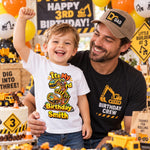 Man with a smiling child wearing a personalised construction-themed third birthday T-shirt at a truck-themed party.