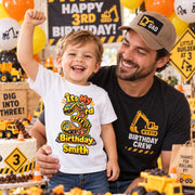 Man with a smiling child wearing a personalised construction-themed third birthday T-shirt at a truck-themed party.