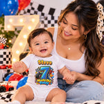 Woman with a smiling baby wearing a personalised 7 months old racing bodysuit beside balloons and a lit number 7.