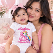 Woman holding a smiling baby wearing a personalised 8 months old unicorn bodysuit and pink bow headband.