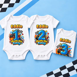 Three white personalised racing milestone bodysuits with blue numbers 1, 2 and 3 on a blue chequered background.